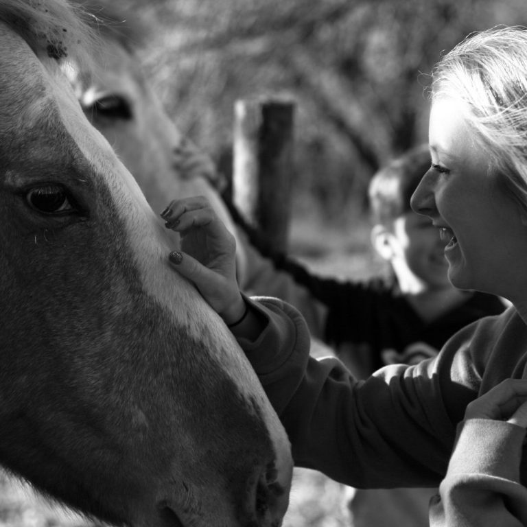 Zwei Kinder streicheln Pferdeköpfe in der Reittherapie, ein lachendes Mädchen vorn im Bild